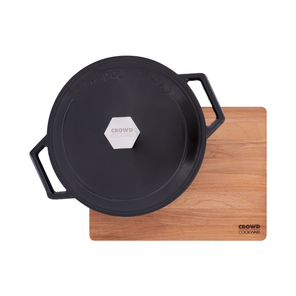 Beech wood rectangular cutting board 40x30 cm with sloped edges, recycled cast iron dutch oven from Crowd Cookware on top in black, and Crowd Cookware logo from top sight